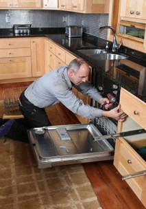 An American Home Appliance technician working on an appliance under a kitchen counter